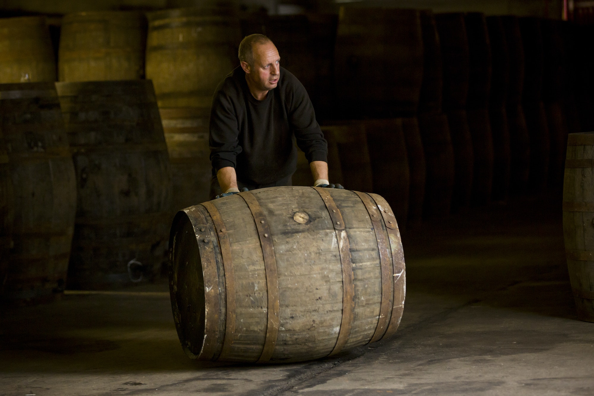 Worker rolling whisky cask in whisky distillery